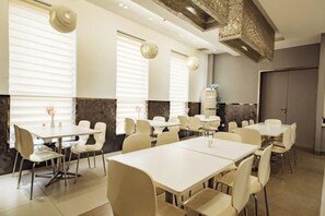 A hotel dining area with multiple tables and chairs, large windows with blinds, and a modern ceiling design. - Jinjiang Inn (Taizhou Wanda Plaza Jiangzhou South Road) (Taizhou)