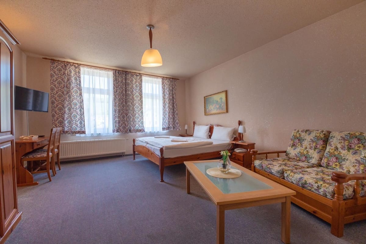 A hotel room with a bed, a sofa, a desk, and a television.