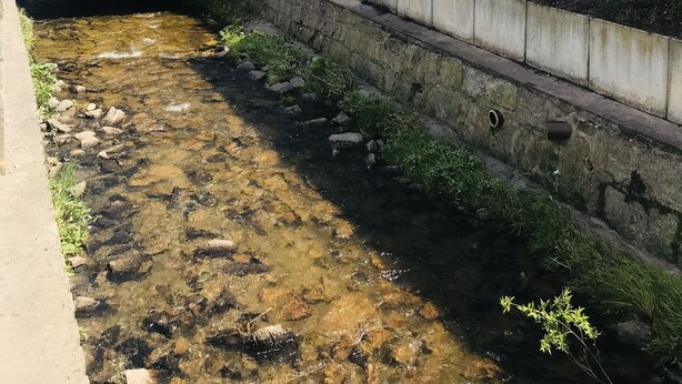 Un hotel a la orilla del río con un puente de madera, muros de piedra y un arroyo de aguas cristalinas.