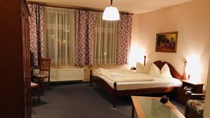 Una habitación de hotel con cama, una silla, una mesa y un radiador.