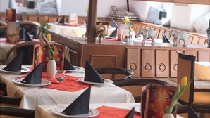 Un restaurante con mesas dispuestas para comer, con servilletas negras, platos blancos y manteles rojos.
