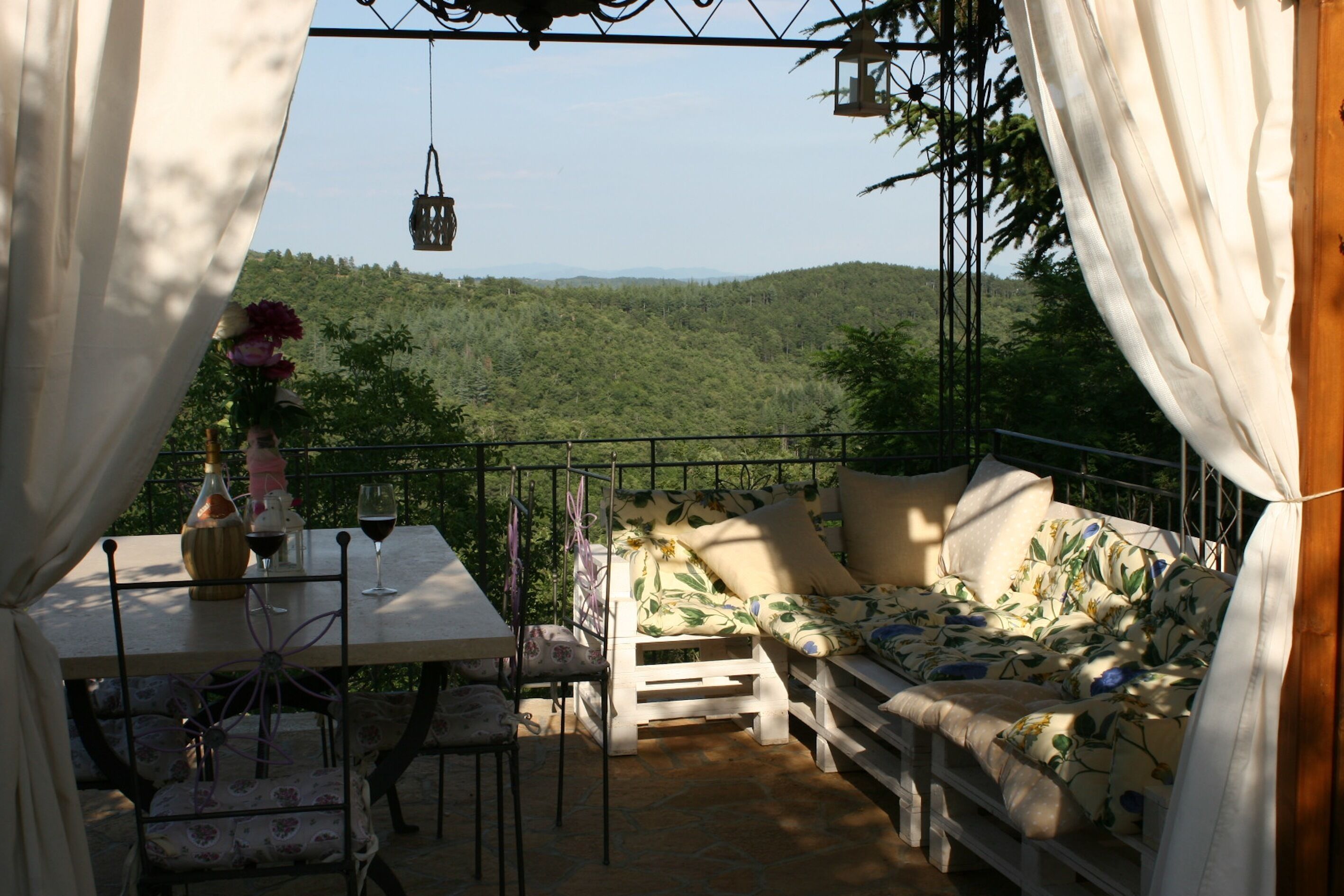 A cozy outdoor seating area with a table, chairs, and a sofa, overlooking a forested hillside.