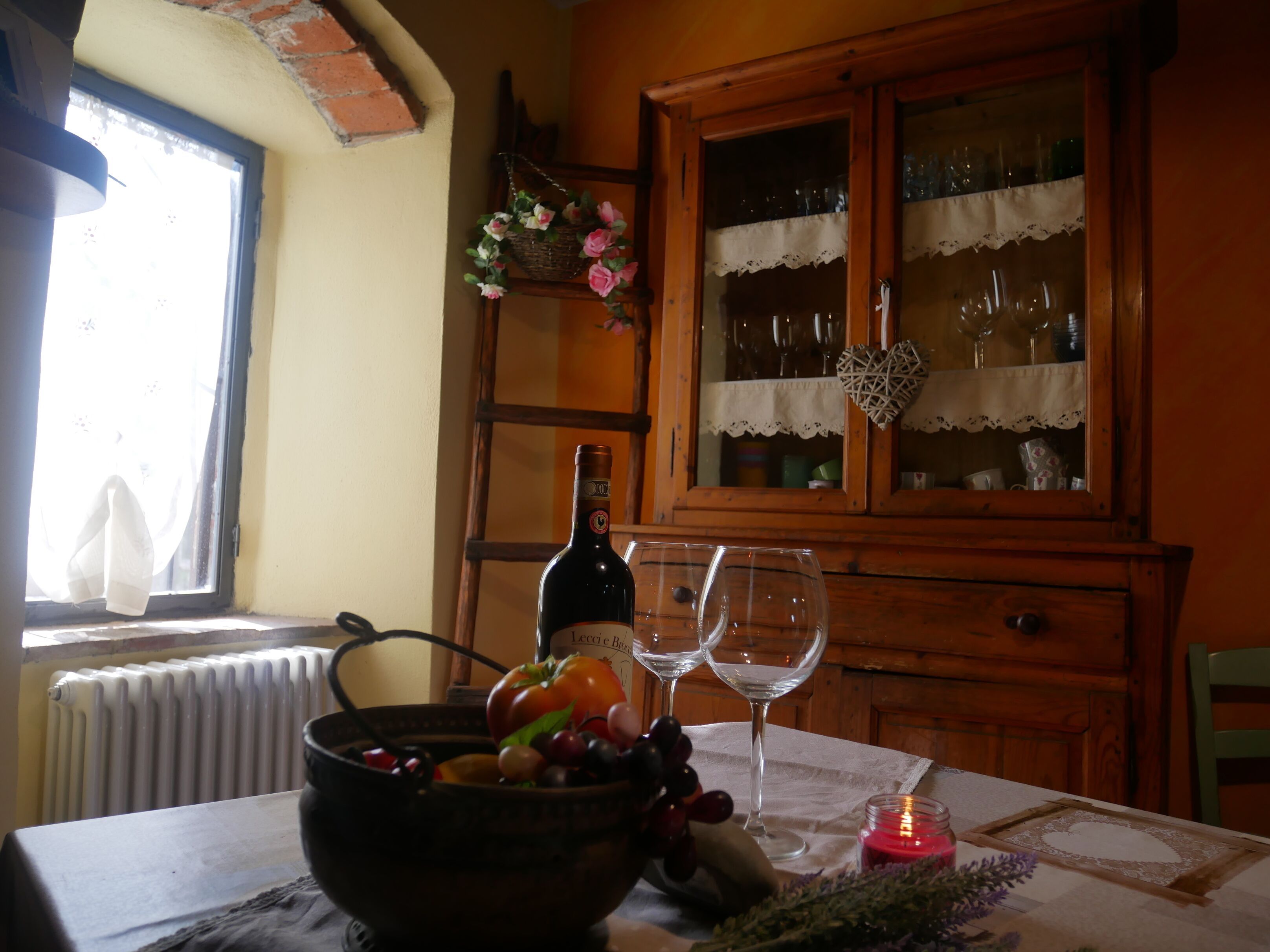 Een eettafel met een fles wijn, twee wijnglazen, een schaal fruit en een kaars.