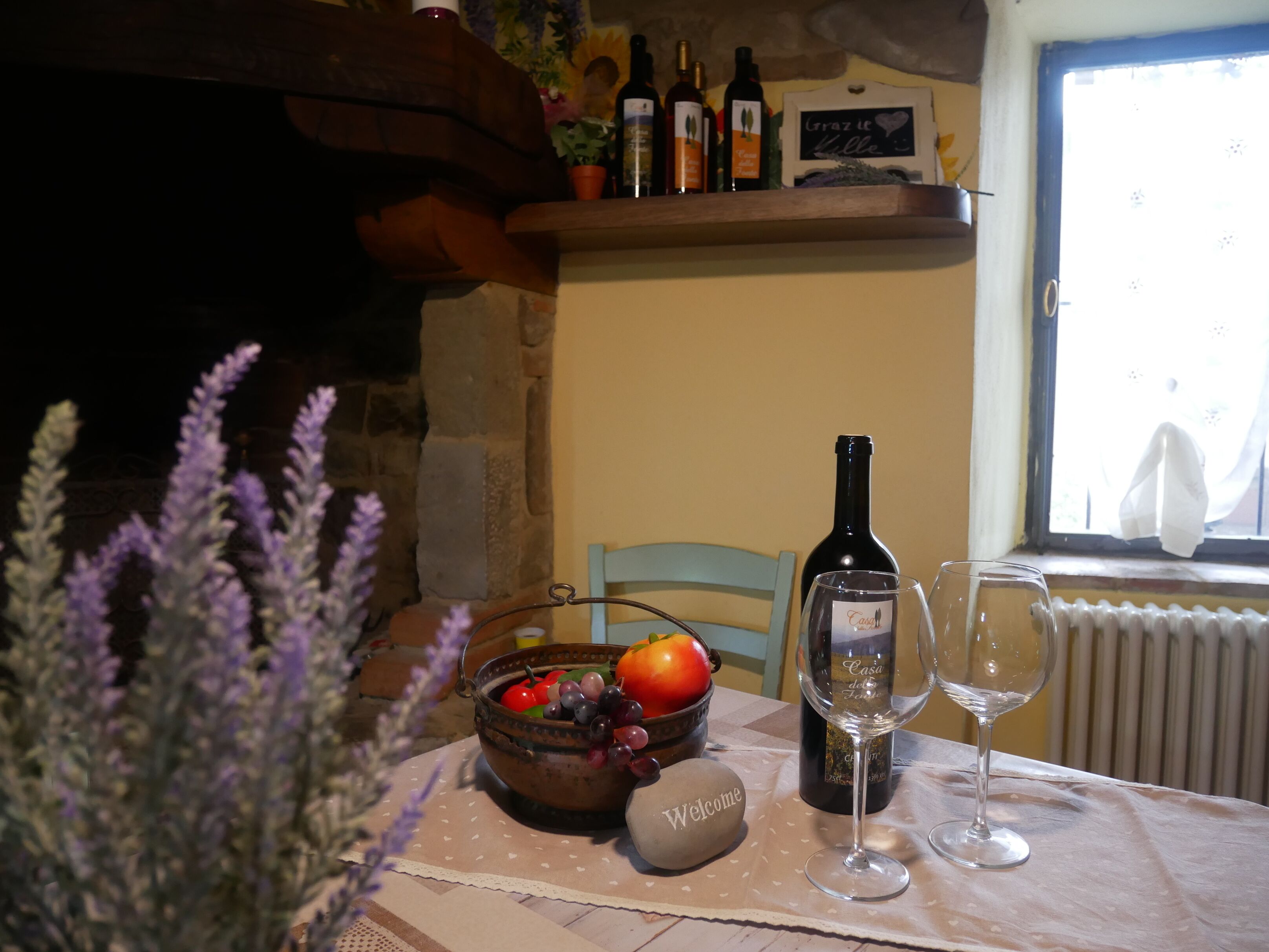 A table with a bottle of wine, two glasses, a bowl of fruit, and a welcome stone.