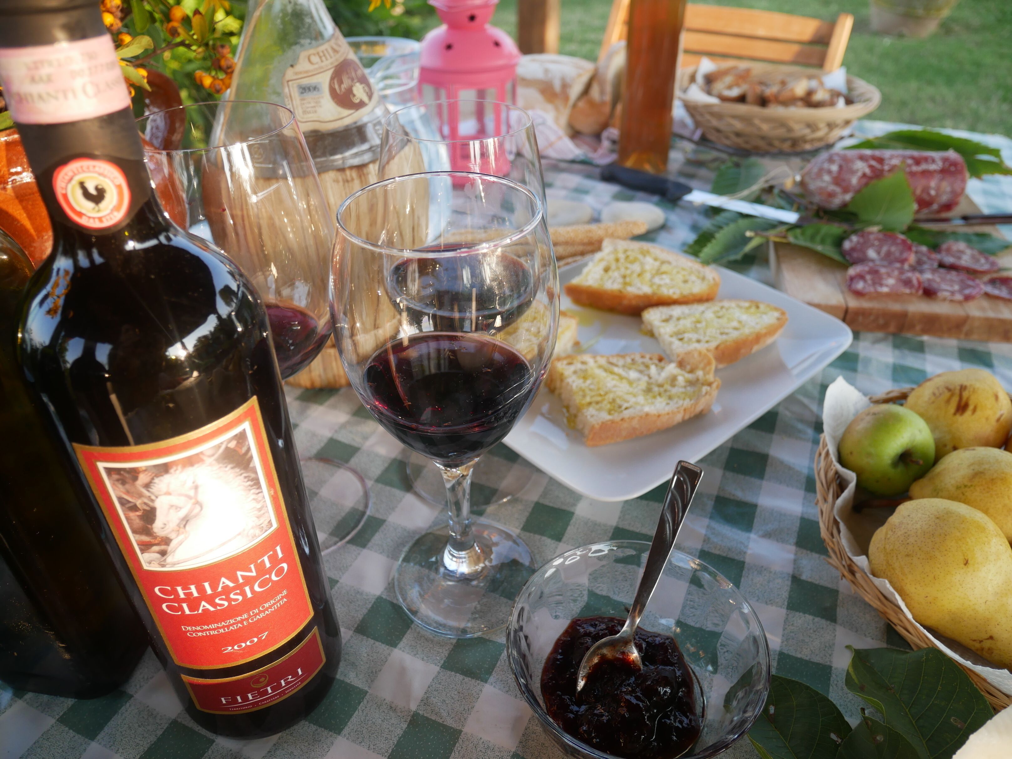 A table set with a bottle of Chianti Classico wine, glasses, bread, cheese, and fruit.