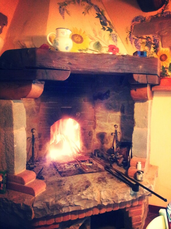 A stone fireplace with a fire burning inside, a wooden mantel above it, and a small shelf with decorative items. - Chianti Holiday House, private jacuzzi up to 6 pax (Fietri)