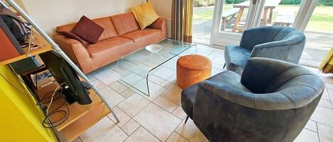 Una sala de estar con sofá, reposapiés y sillones, una mesa de centro de vidrio y un reloj de pared.