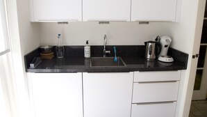 Une cuisine avec des meubles blancs, un plan de travail noir, un évier en acier inoxydable, une machine à café et un flacon de savon liquide.