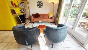 Un salon comprenant un canapé, deux fauteuils, une table basse, une bibliothèque et une grande fenêtre.