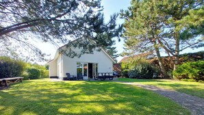 Un bâtiment blanc avec un toit en pente, un patio couvert doté de sièges extérieurs et une pelouse bien entretenue.