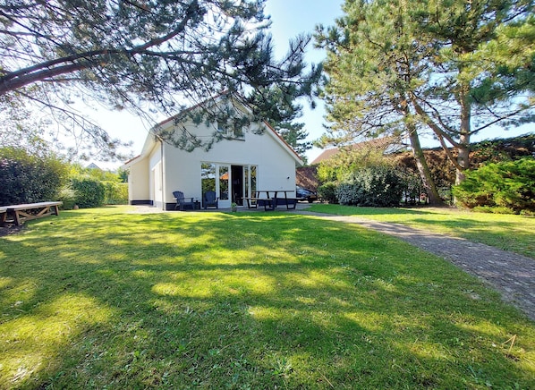A white building with a sloped roof, a covered patio with outdoor seating, and a well-maintained lawn.