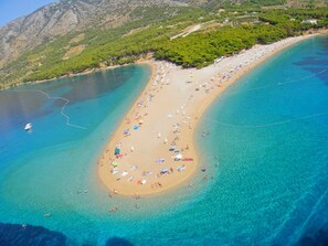 An aerial view of a beach with clear turquoise waters, a sandy shore, and a mountainous backdrop. - Apartments Olga, (12629), Bol, hr (Bol)