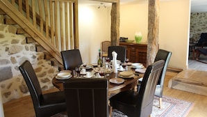 A dining area with a stone wall, wooden staircase, and a dining table set with plates, glasses, and chairs.