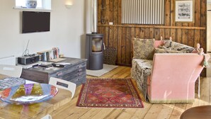 A cozy living room with a wooden floor, a sofa, a coffee table, a fireplace, and a television mounted on the wall.