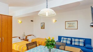 Una habitación con una mesa de comedor, dos camas, un sofá azul y una lámpara colgante.