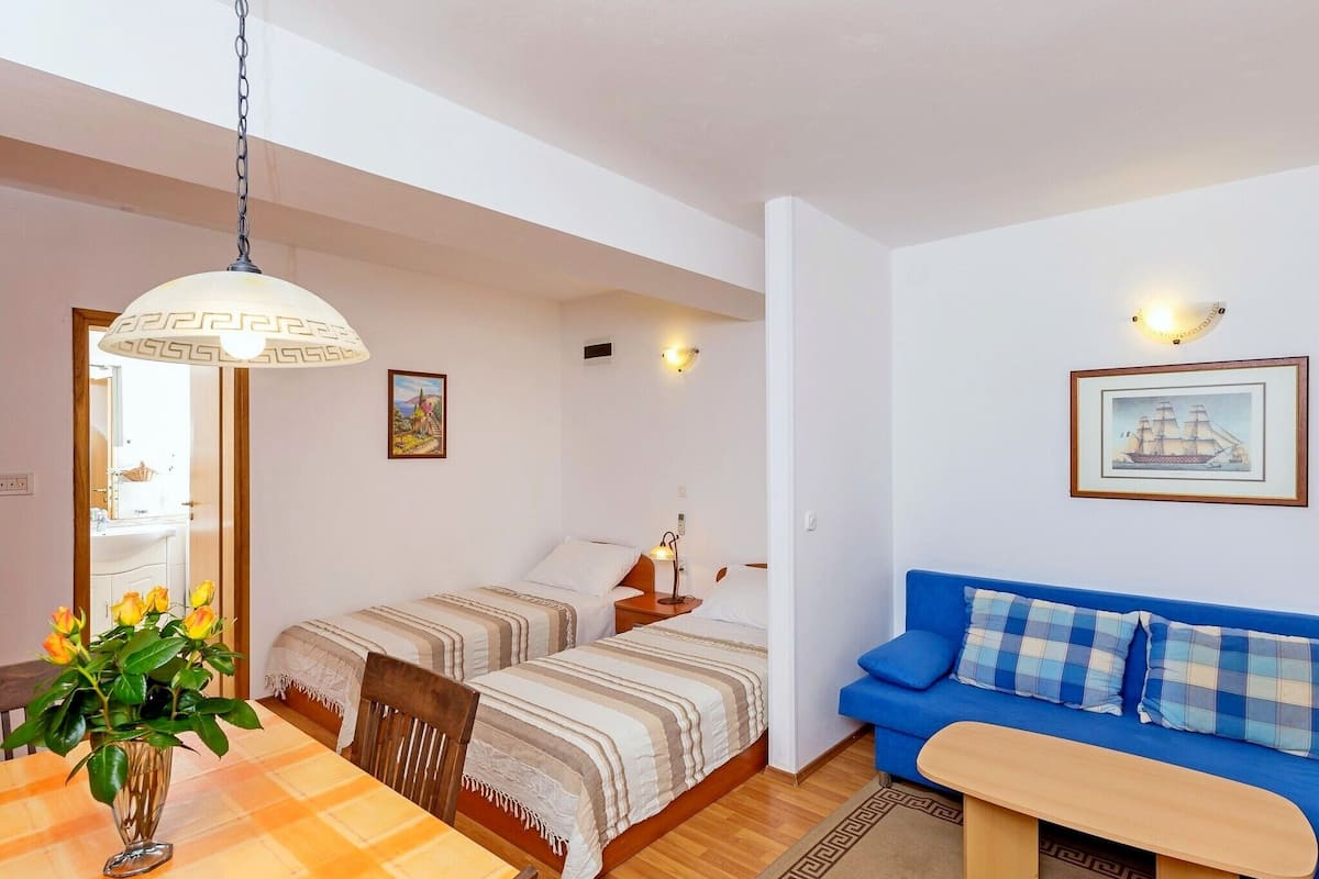 A cozy room with two beds, a dining table with a vase of flowers, a blue sofa, and a small wooden table.