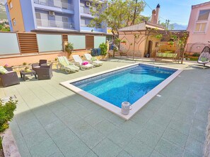 A rectangular swimming pool with a tiled deck, surrounded by lounge chairs and a small table with a drink. - Apartments Ivan, (15798), Solin, hr (Solin)
