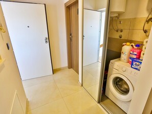 A laundry area with a washing machine, a glass door, and cleaning supplies. - Apartments Ivan, (15798), Solin, hr (Solin)