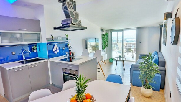 A modern kitchen with a central island, a dining area with a table set for two, and a balcony with outdoor seating. - Apartments Ivan, (15797), Solin, hr (Solin)