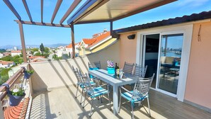 A balcony with a table and chairs, a potted plant, and a view of the city. - Apartments Ivan, (15797), Solin, hr (Solin)
