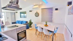 A modern kitchen with a built-in oven, a dining area with a white table and blue chairs, and a blue sofa in the living area. - Apartments Ivan, (15797), Solin, hr (Solin)