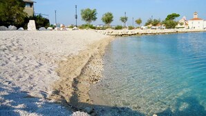 A beach with clear water, a rocky shoreline, and buildings in the background. - Apartments Ivan, (15797), Solin, hr (Solin)