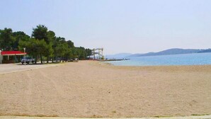 A beach with a clear sky, a few trees, and a distant view of mountains. - Apartments Kristina, (15936), Vodice, hr (Vodice)
