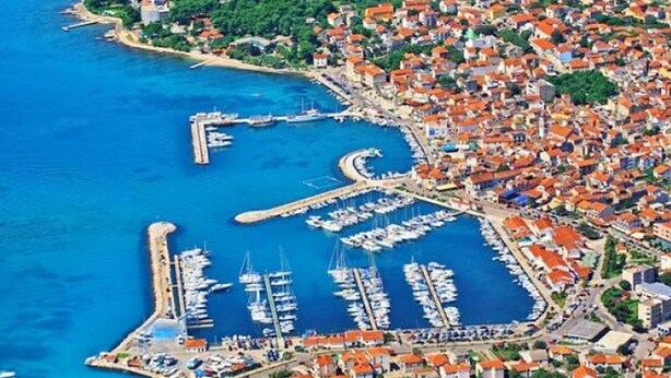 An aerial view of a coastal town with a marina, dense housing, and a prominent hill with greenery. - Apartments Kristina, (15936), Vodice, hr (Vodice)