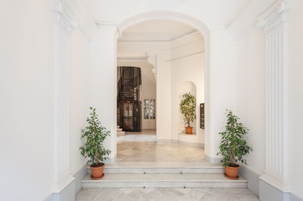 A grand entrance with a marble floor, a staircase, and two potted plants.