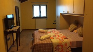 A bedroom with a bed, a television on a stand, a window, and a radiator.