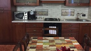A kitchen with wooden cabinets, a microwave, a stove, and a dining table with a colorful tablecloth.