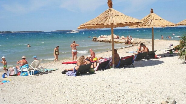 Una playa con sombrillas, tumbonas y gente disfrutando del agua.