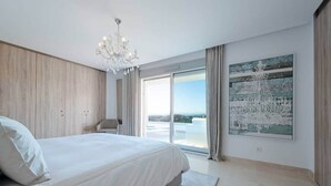 Een moderne slaapkamer met een groot bed, een kroonluchter, uitzicht op de omgeving en een groot kunstwerk aan de muur.