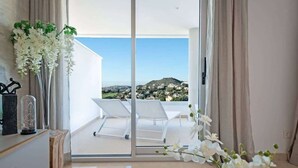 Een moderne kamer met balkon, witte stoelen en uitzicht op een heuvel.
