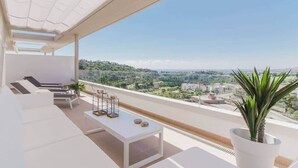 Een modern balkon met witte meubels, een tafel en een plant in een pot, met uitzicht op een schilderachtig landschap.