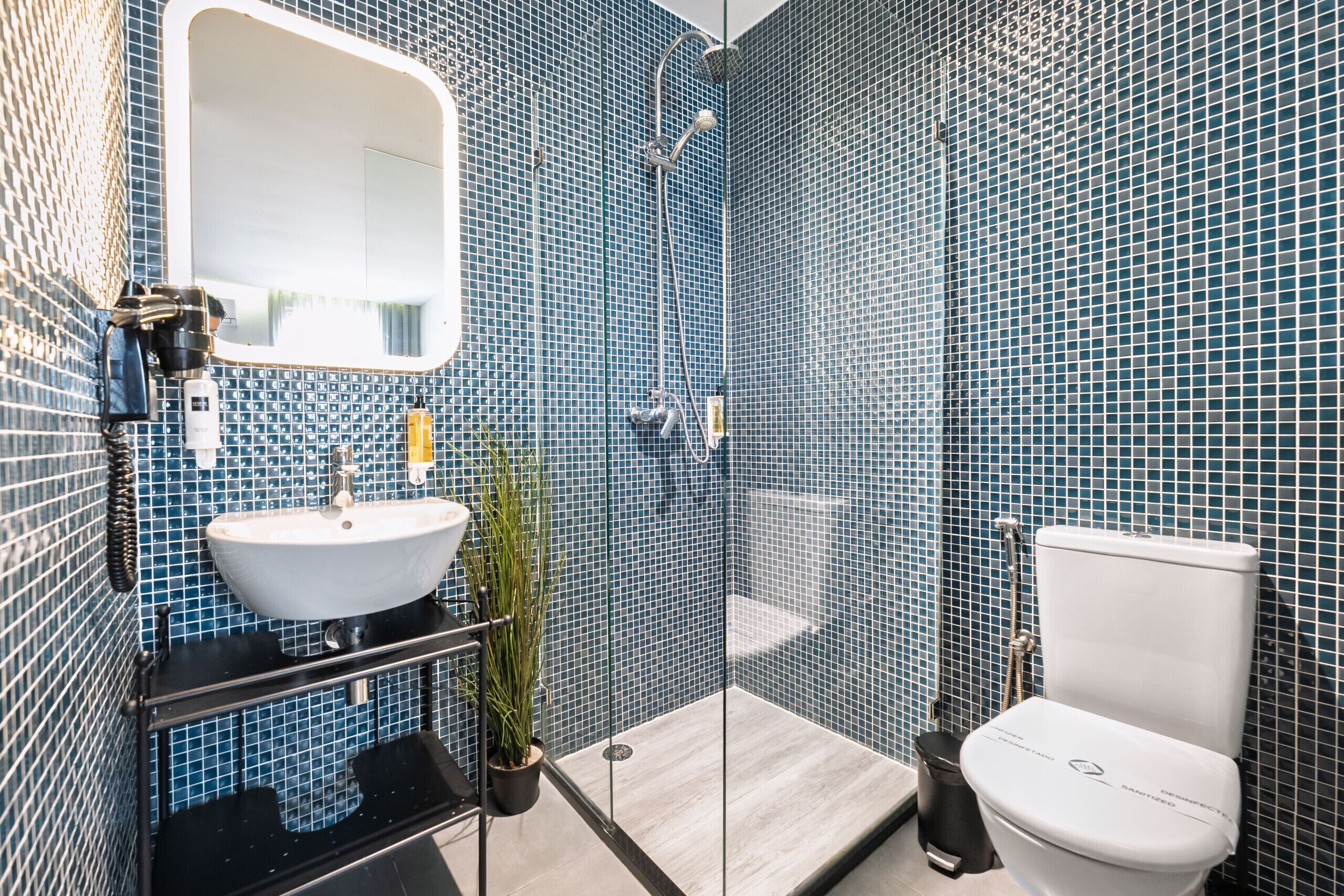 A modern bathroom with a white sink, mirror, and toilet, surrounded by blue mosaic tiles.