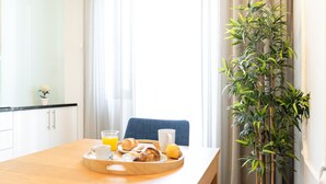 Ein Frühstückswagen mit Croissants, einem Glas Orangensaft und einer Tasse auf einem Holztisch in einem hellen Raum mit Blumentopf und Vorhängen.