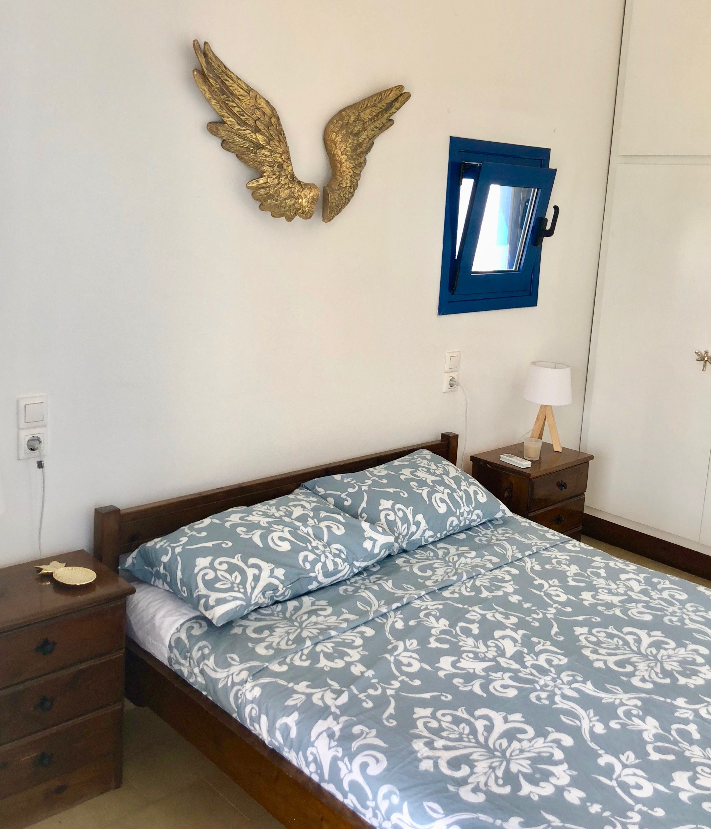 A bedroom with a bed, wooden nightstands, a lamp, and a wall-mounted window.
