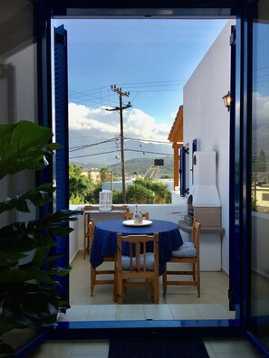 An outdoor dining area with a table and chairs, a white outdoor kitchen, and a view of the surrounding landscape. - Aphrodite and Apollo Apartments (Agios Nikolaos)