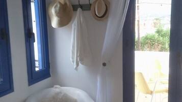 A room with a white armchair, a small table, a hat rack with hats, and a view of an outdoor area with a yellow chair.
