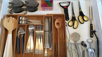 Un cajón con diversos utensilios de cocina, incluyendo espátulas, cucharas, tenedores, cuchillos y un rallador.