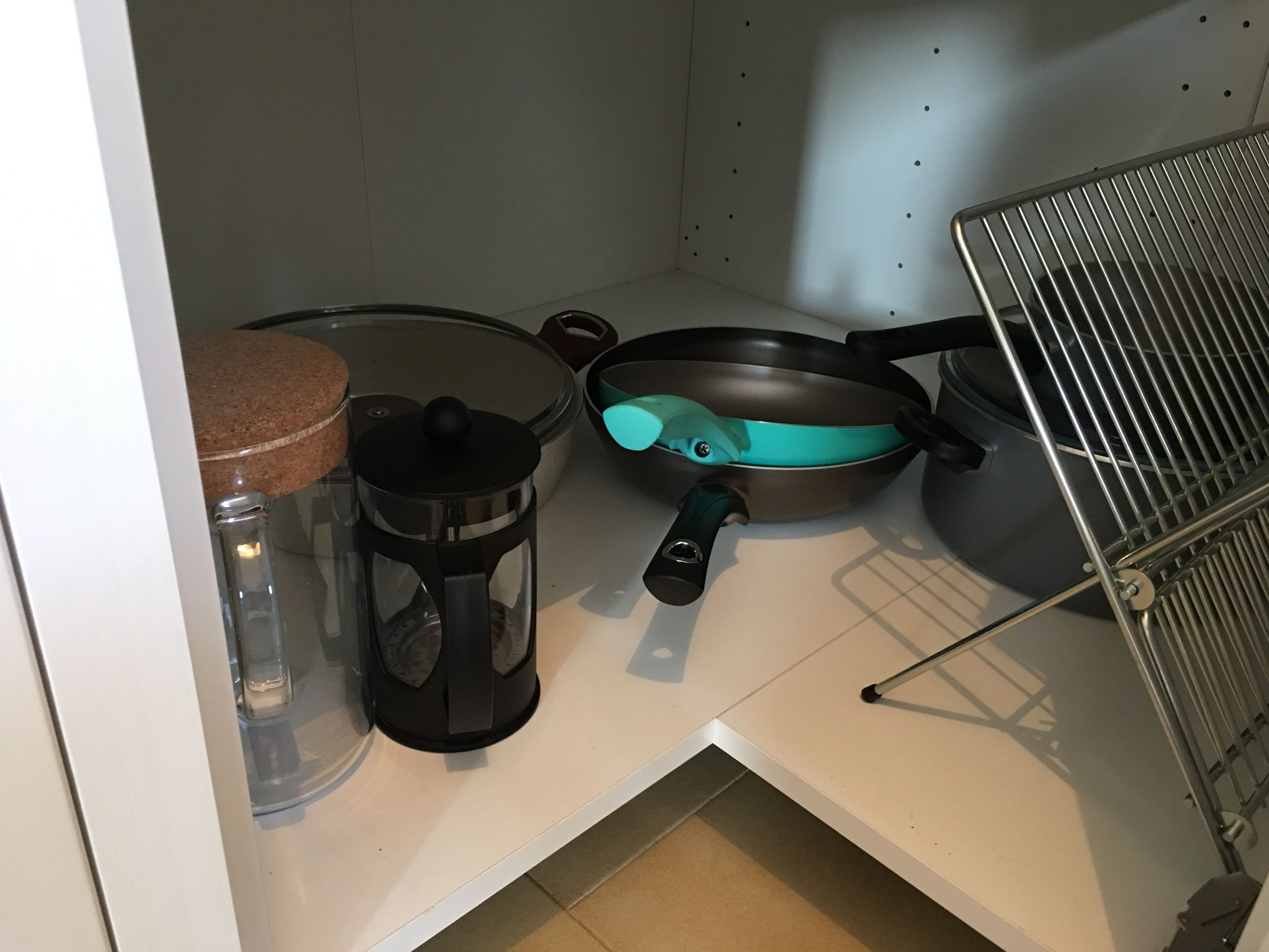 A kitchenette with a coffee maker, a frying pan, a pot, and a kettle on a white countertop.