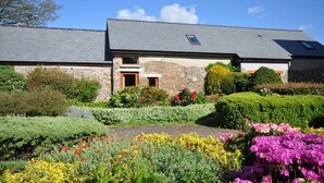 A stone building with a grey roof, surrounded by well-maintained gardens with various flowers and shrubs. - Montgomery Barn at High Park, Indoor Pool (Devon)