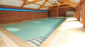 An indoor swimming pool with a tiled floor and a wooden ceiling structure. - Montgomery Barn at High Park, Indoor Pool (Devon)