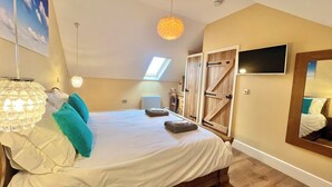 A bedroom with a large bed, a skylight, a wooden wardrobe, a television, and a chandelier. - Montgomery Barn at High Park, Indoor Pool (Devon)