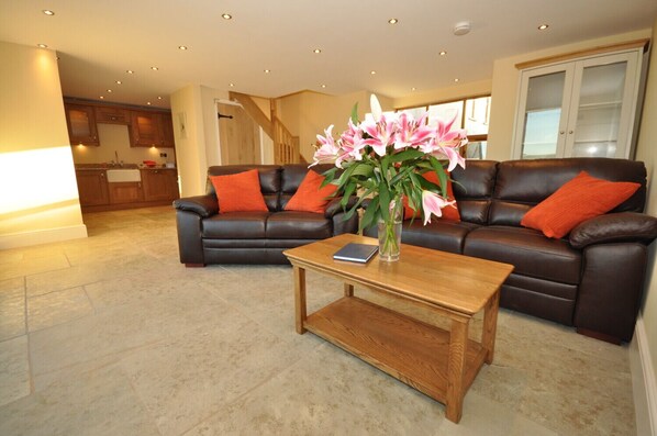 A living room with a brown leather sofa, a wooden coffee table, and a vase with flowers. - Montgomery Barn at High Park, Indoor Pool (Devon)