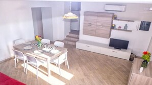 A modern dining area with a table set for four, a staircase leading to another level, a TV on a white cabinet, and a small plant on the right. - Paola Vico Equense house (Vico Equense)