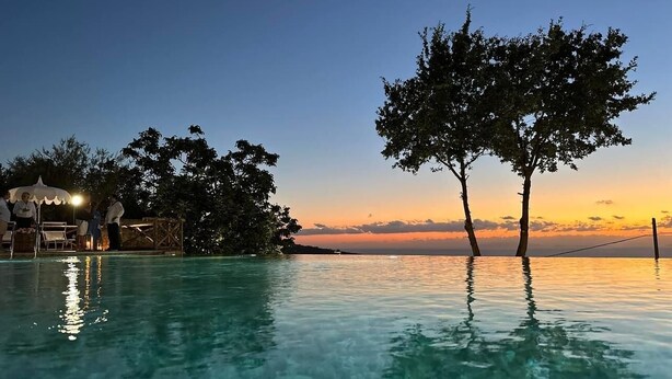 An infinity pool with clear water reflecting the sky, surrounded by trees and a sunset view. - Paola Vico Equense house (Vico Equense)