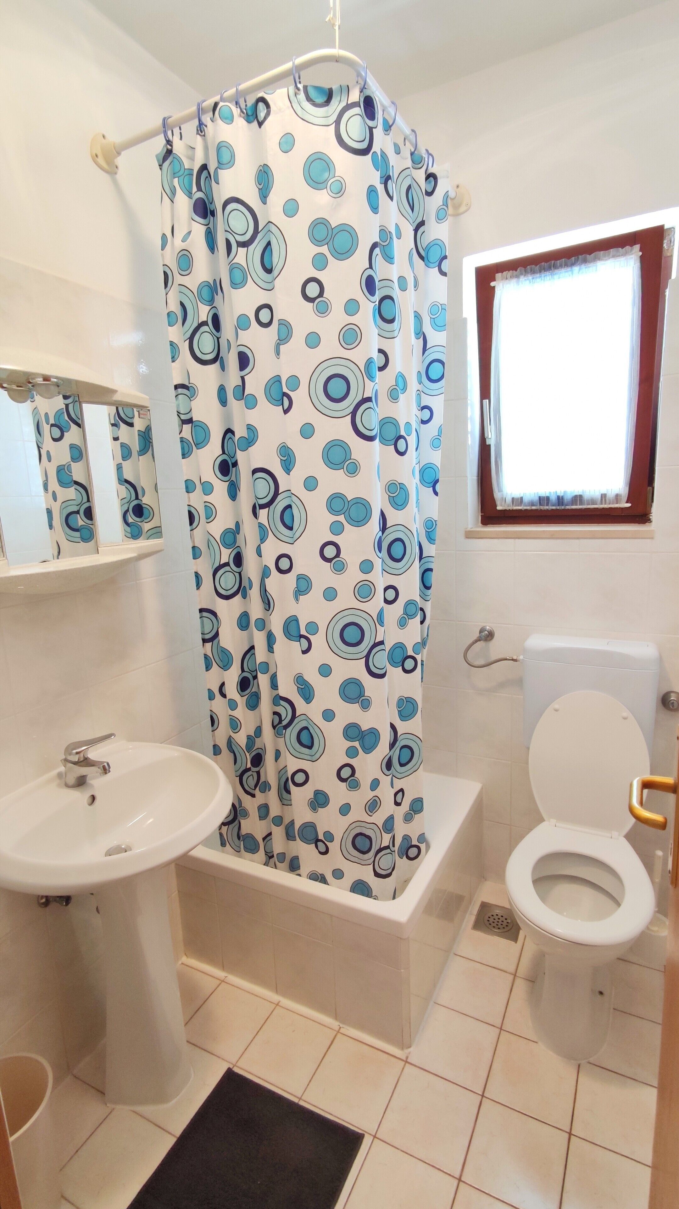 Ein Badezimmer mit Duschvorhang, Waschbecken, Toilette und Fenster.