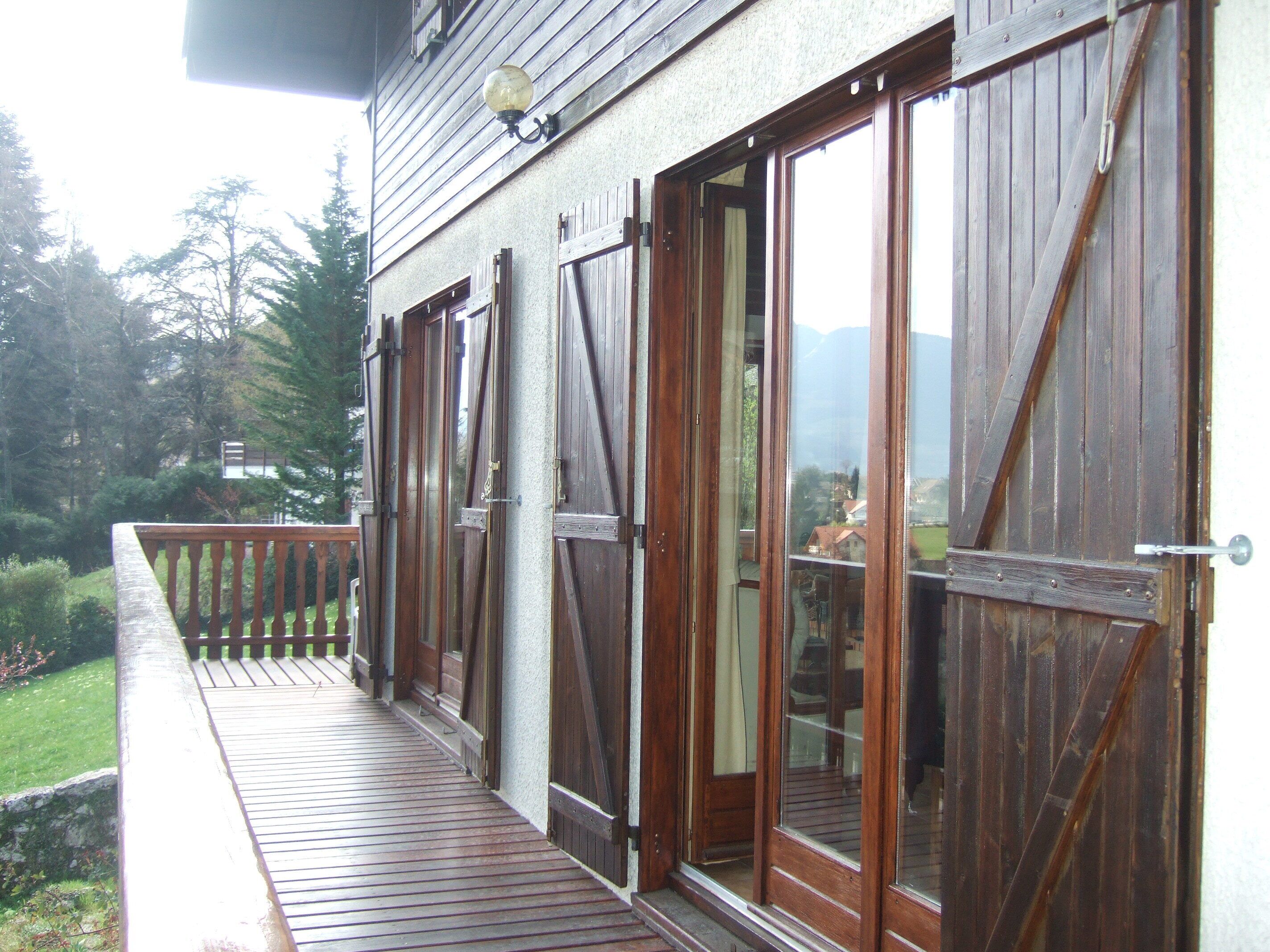 Un balcone in legno con ringhiera, una porta e una finestra anch'esse in legno.
